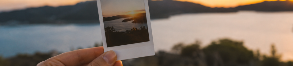 mão segurando foto impressa instantânea durante o pôr do sol com paisagem ao fundo