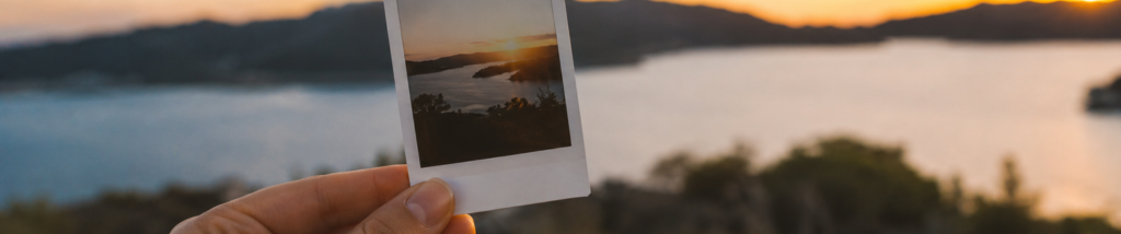 mão segurando foto impressa instantânea durante o pôr do sol com paisagem ao fundo